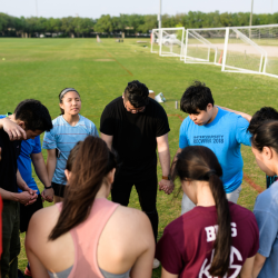 students standing in a prayer circle on a field