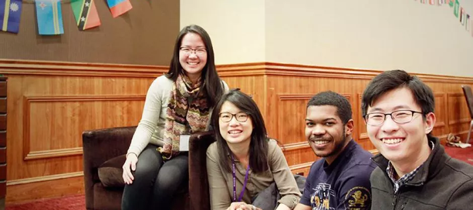 A group of students smiling. Behind them are flags from many different nations.