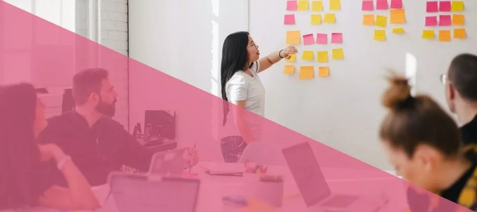 Person in front of room leading a meeting with sticky notes on the wall.