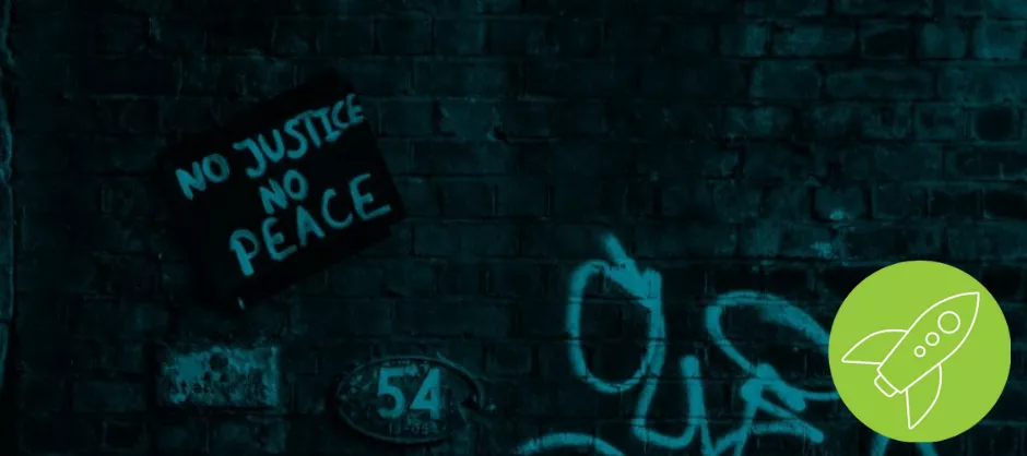 Dark cyan brick wall with a sign propped up reading "No Justice No Peace"