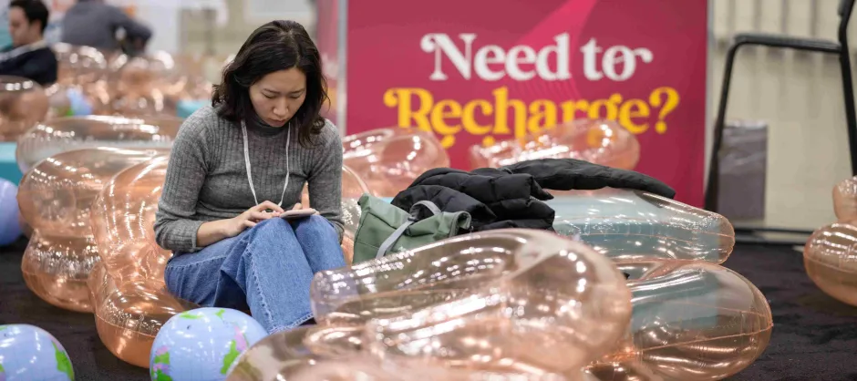 A student sits on an inflatable tube with the words on a poster behind them saying "Need to Recharge?"