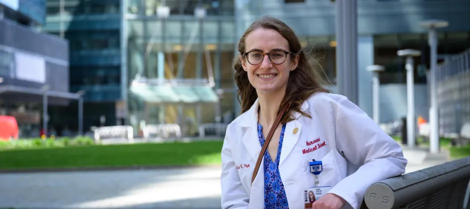 A brown haired woman smiling at the camera. She is wearing a white lab coat for Medical school.