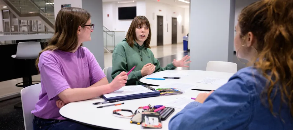 Three students at a table discussing.