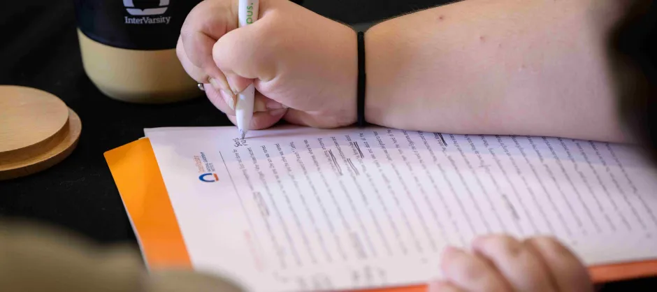 A person focused on writing notes on a paper manuscript with a pen in hand.
