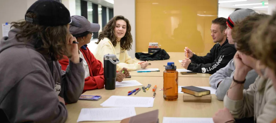 A diverse group of people engaged in conversation around a table, sharing ideas during Bible Study..
