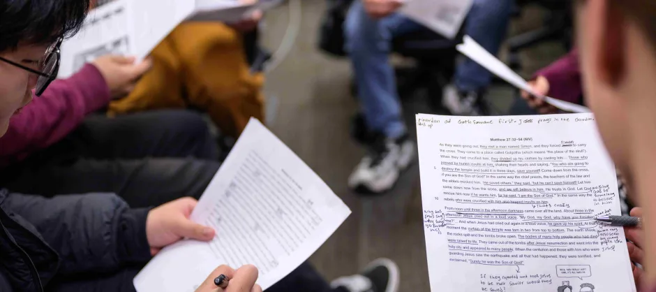 Students collaborating at a table, surrounded by Bible manuscripts, focused on their discussions.