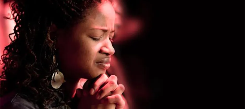 A black woman with black braids and big earrings praying.