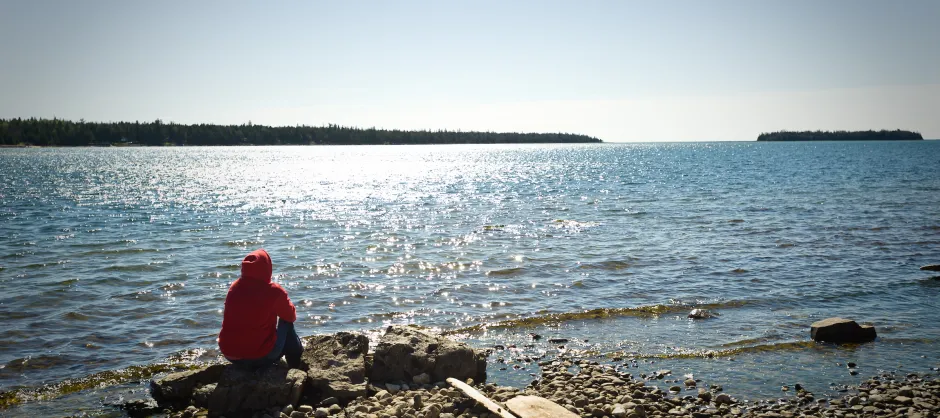A college student sitting and looking out over a body of water.