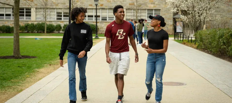 3 college students walking alongside eachother. One is gesturing to the others with her hands.