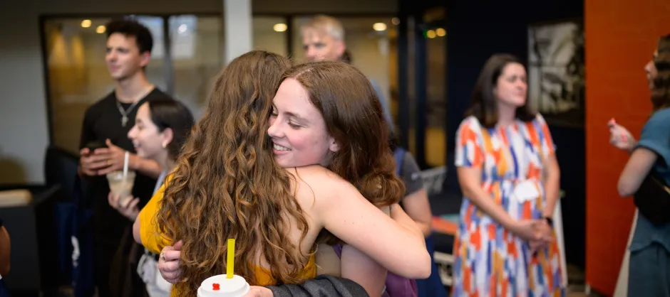 Two women hugging in a crowded room.