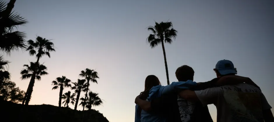 three people hugging on the side looking into the sunset