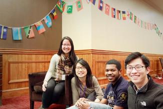 A group of students smiling. Behind them are flags from many different nations.