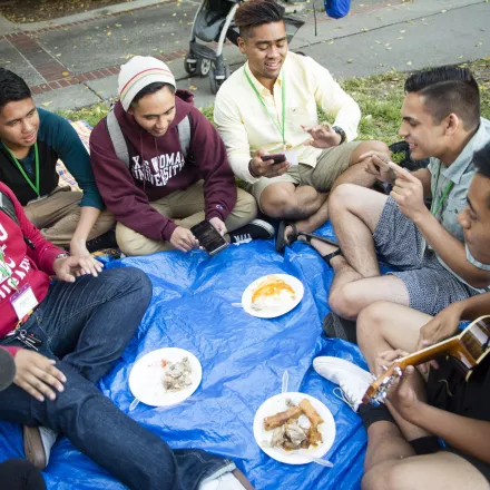 A group of students of East and SouthEast Asian descent sitting in a circle eating and playing music.
