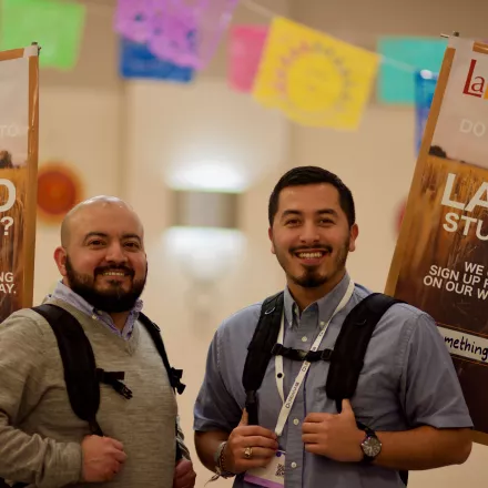 Two latino males with backpacks smiling at camera with a background of papel picado